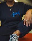 Woman wearing Blue Jersey Love Tee in Black sitting on a large red box. Wakefield District streetwear fit showing clear blue Jersey graphic from the Contant Avenue collection.
