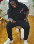 man wearing black jersey script t-shirt with pink logo sitting indoors casual relaxed fit