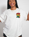 Female model with braided hair smiling and wearing the white Eight Seven Six Scribble Tee, showcasing the relaxed fit and the custom 876 chest graphic. Studio photograph with a cohesive warm, grained film aesthetic.