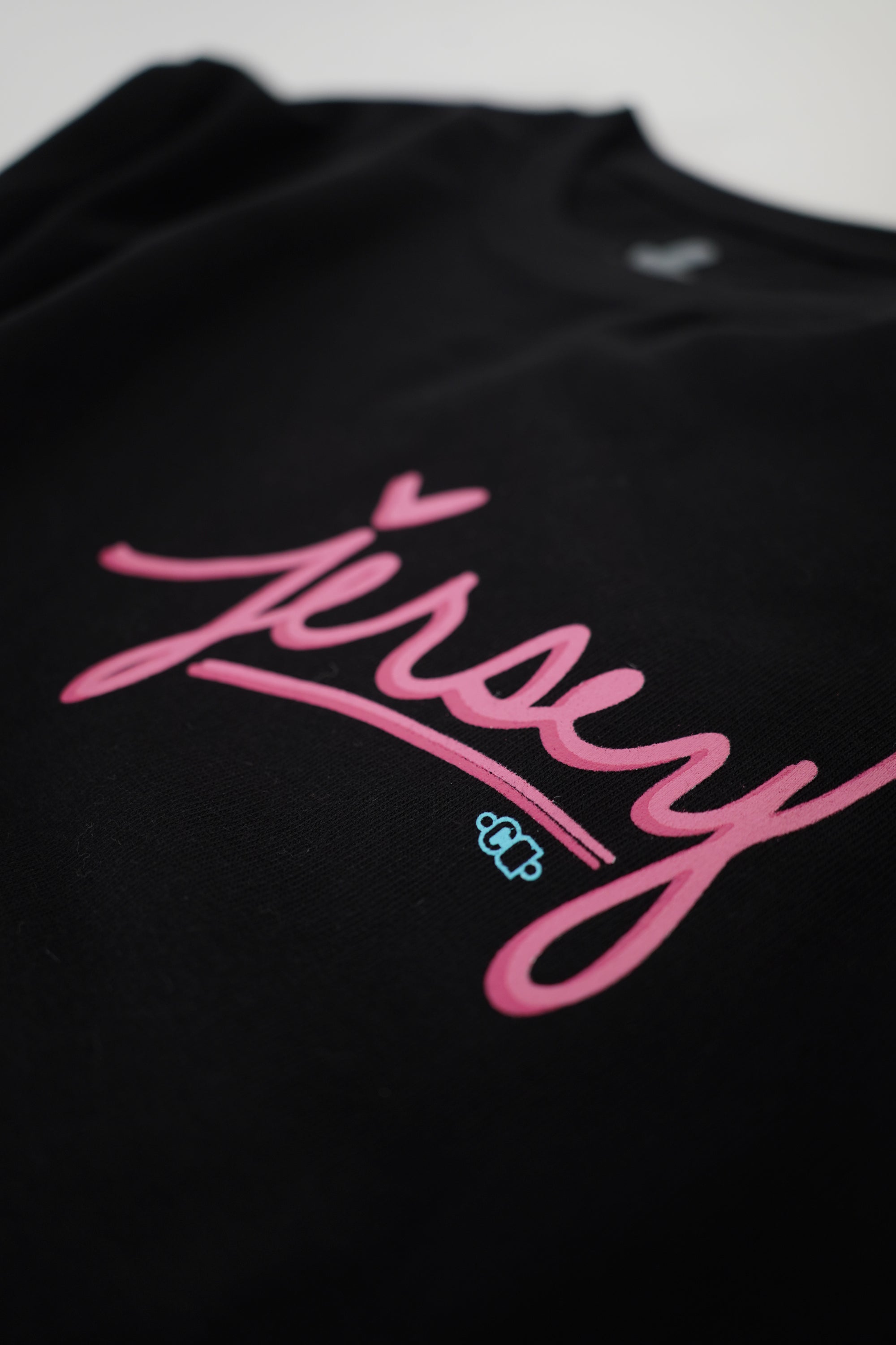 Close-up detail of bold pink screenprint graphic on black heavyweight cotton tee by Wakefield District. Premium quality texture.