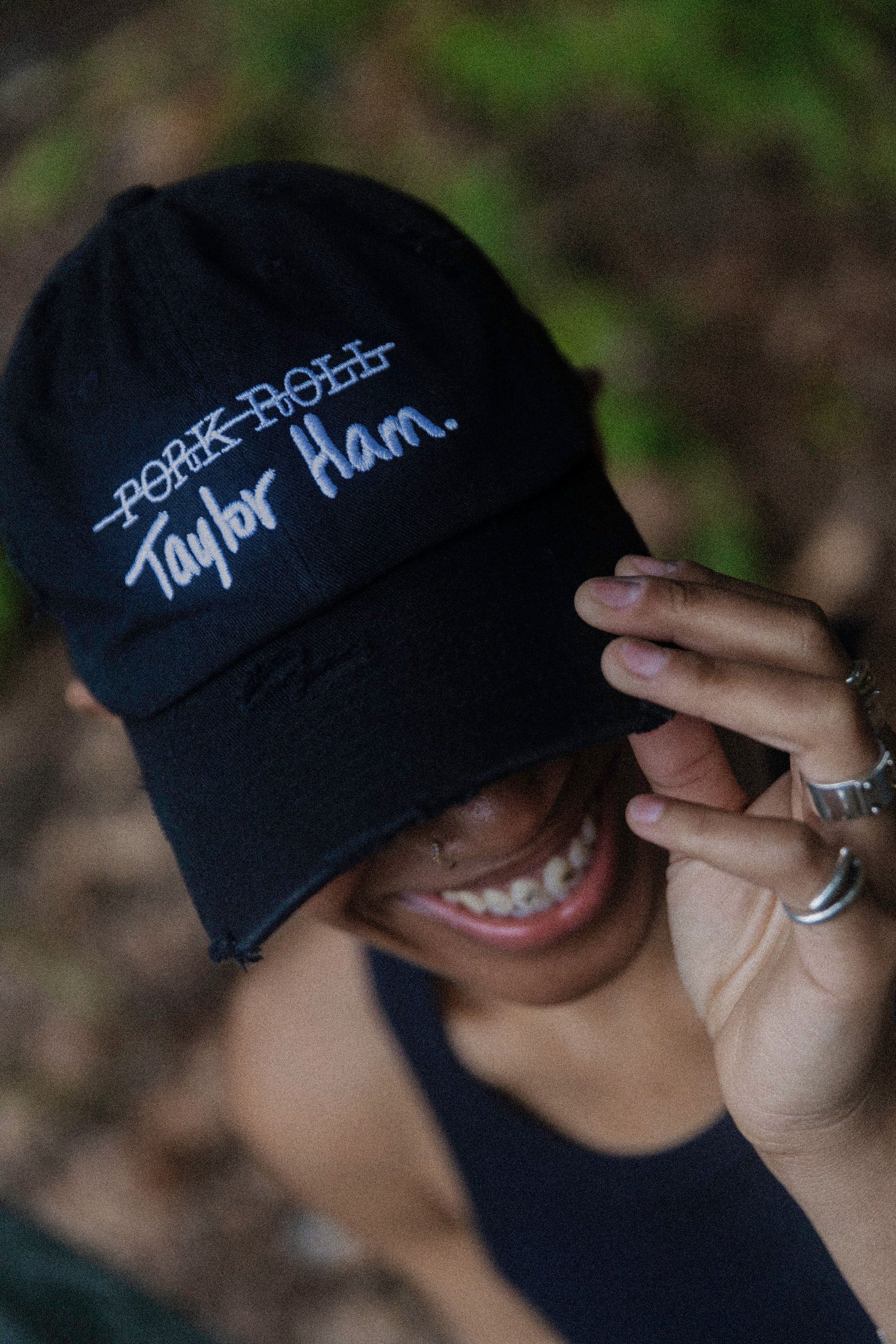 Model wearing the black distressed Signature Taylor Ham Hat by Wakefield District. A staple from the Contant Avenue collection. Grainy, outdoor streetwear lifestyle portrait highlighting the Jersey debate graphic.