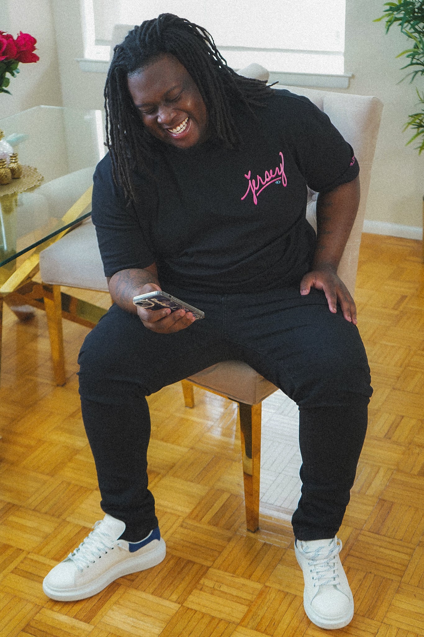 man wearing black jersey script t-shirt with pink logo sitting indoors casual relaxed fit