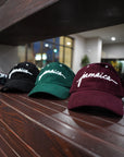 Three Wakefield District Jamaica Corduroy Hats in Black, Jasper Green, and Garnet Red displayed on a wooden ledge. The editorial film-grain style showcases the full color range of the collection.