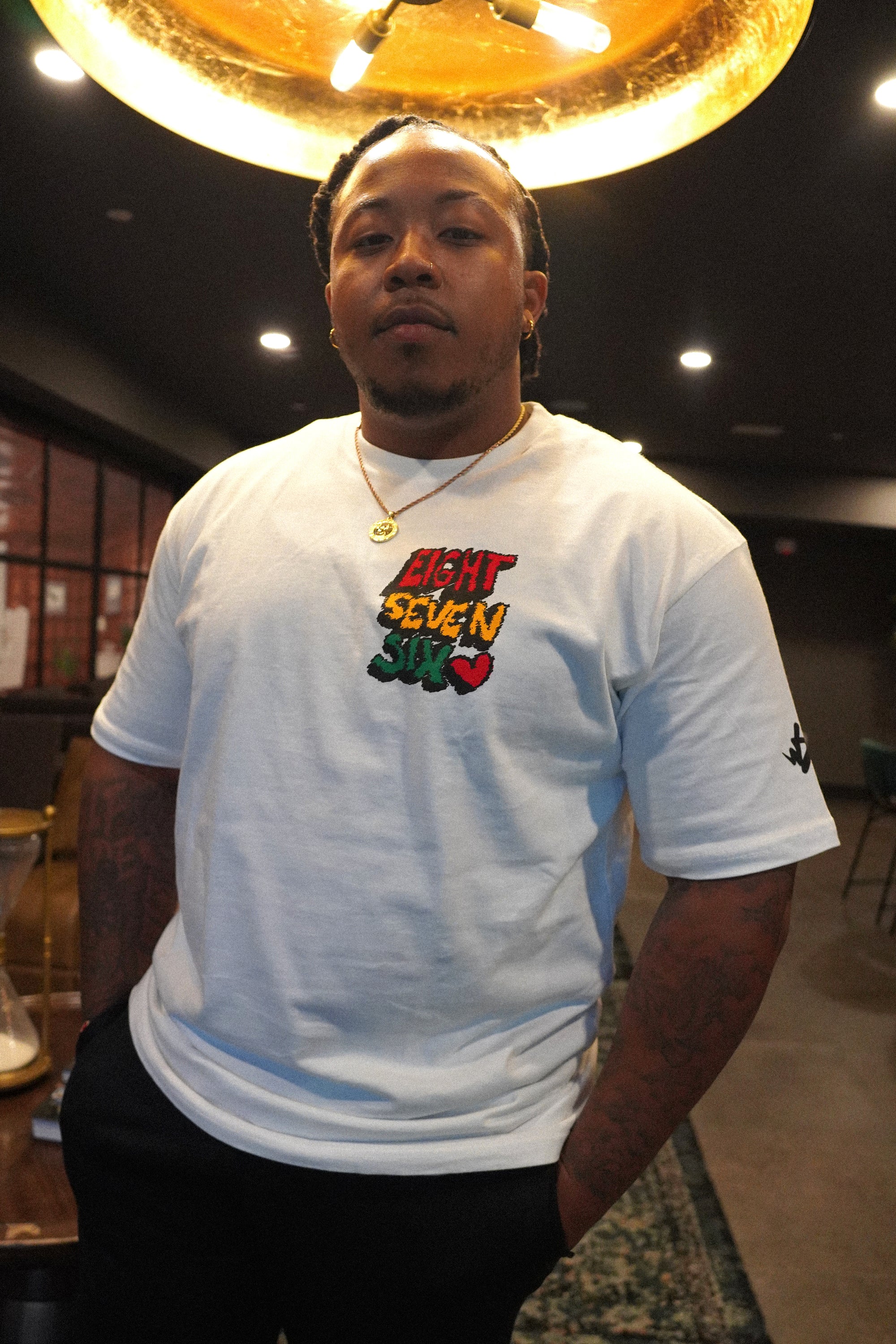 Male model wearing the Wakefield District Eight Seven Six Scribble Tee in white, showing the relaxed fit and the custom hand-drawn 876 chest graphic. Shot indoors with a warm editorial aesthetic.