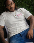 Man wearing natural color t-shirt with pink Jersey script graphic sitting outdoors