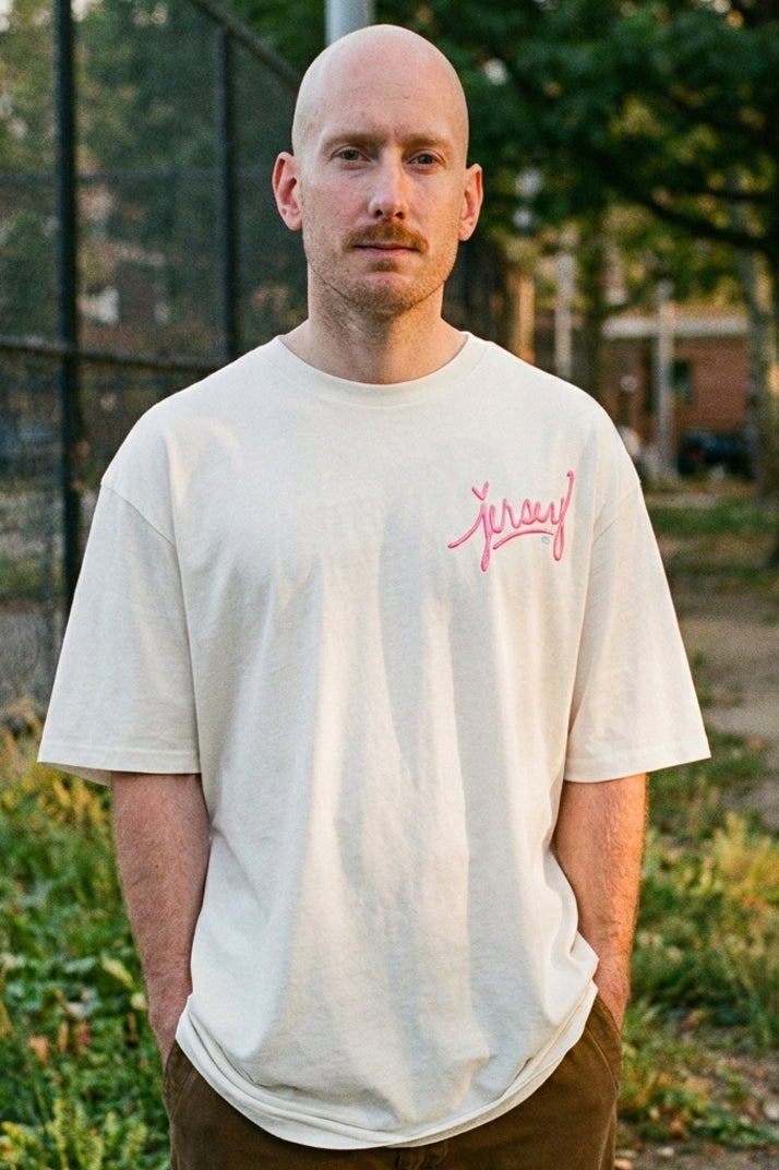 Man wearing the Wakefield District Pink Jersey Love Tee in Natural from the Contant Avenue subcollection. Unisex streetwear fit in cream heavyweight cotton with pink graphic.